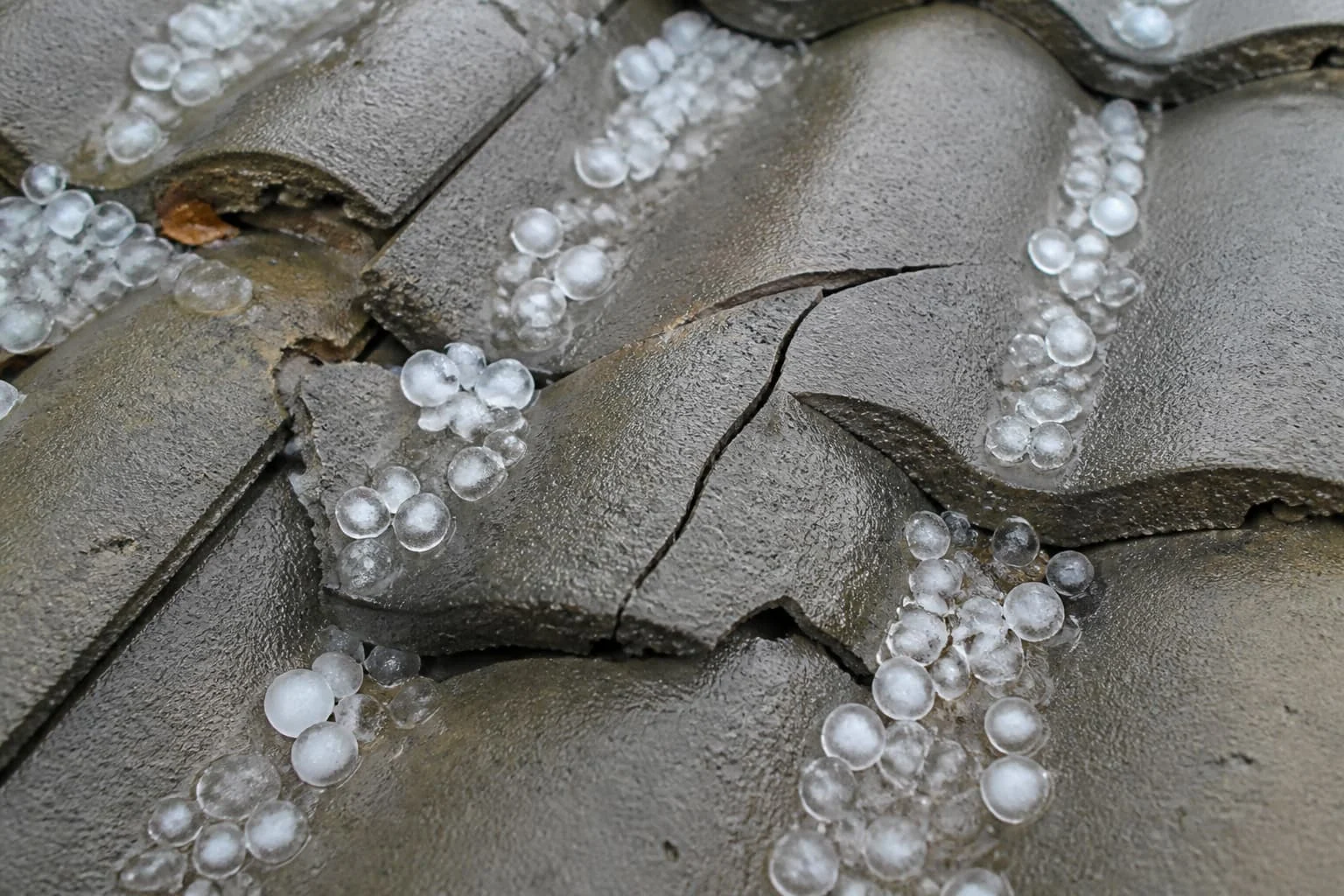 Illustration of hailstones on cracked gray concrete roof tiles