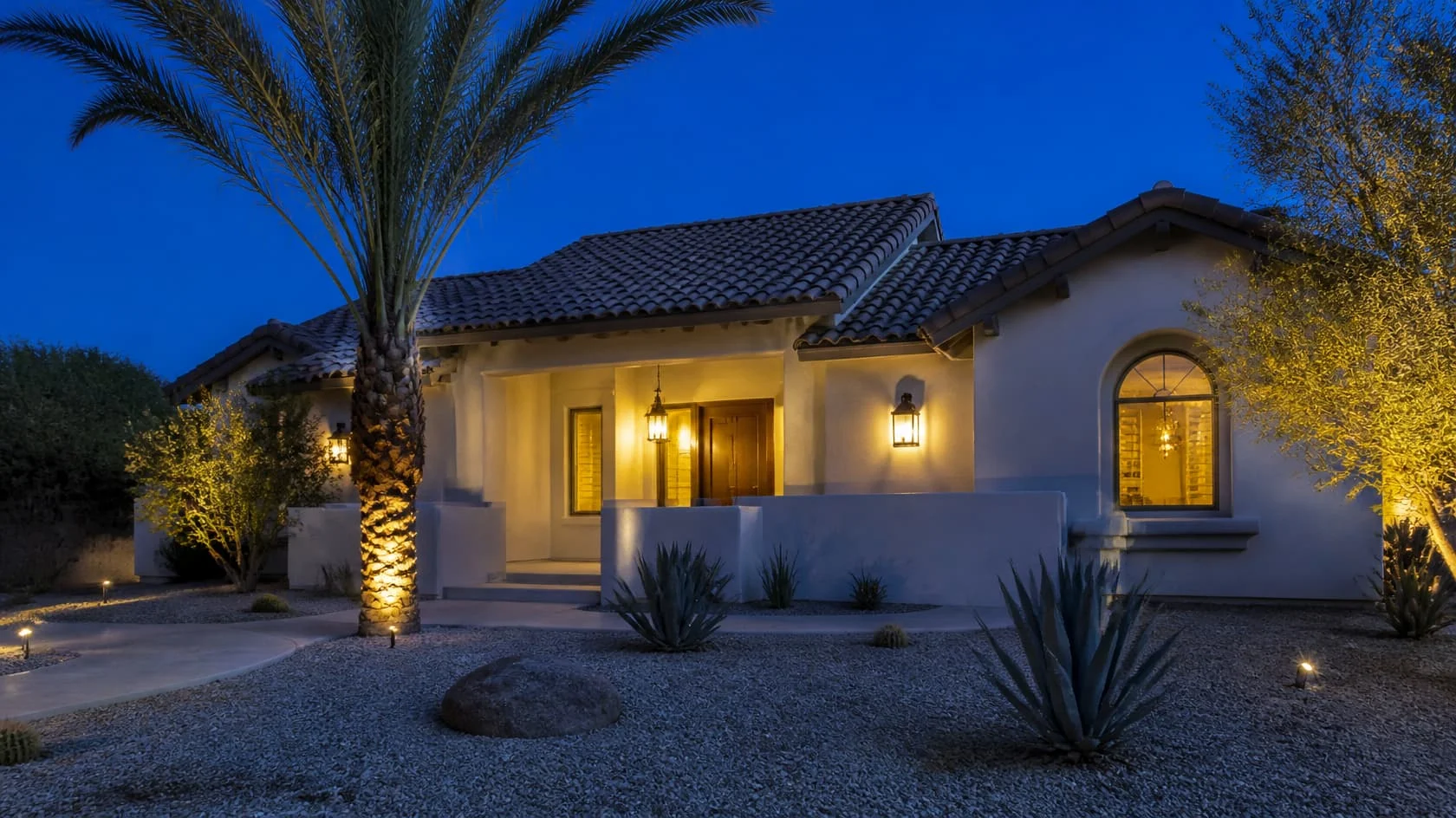 White tile roof home with warm lights and palms at blue hour