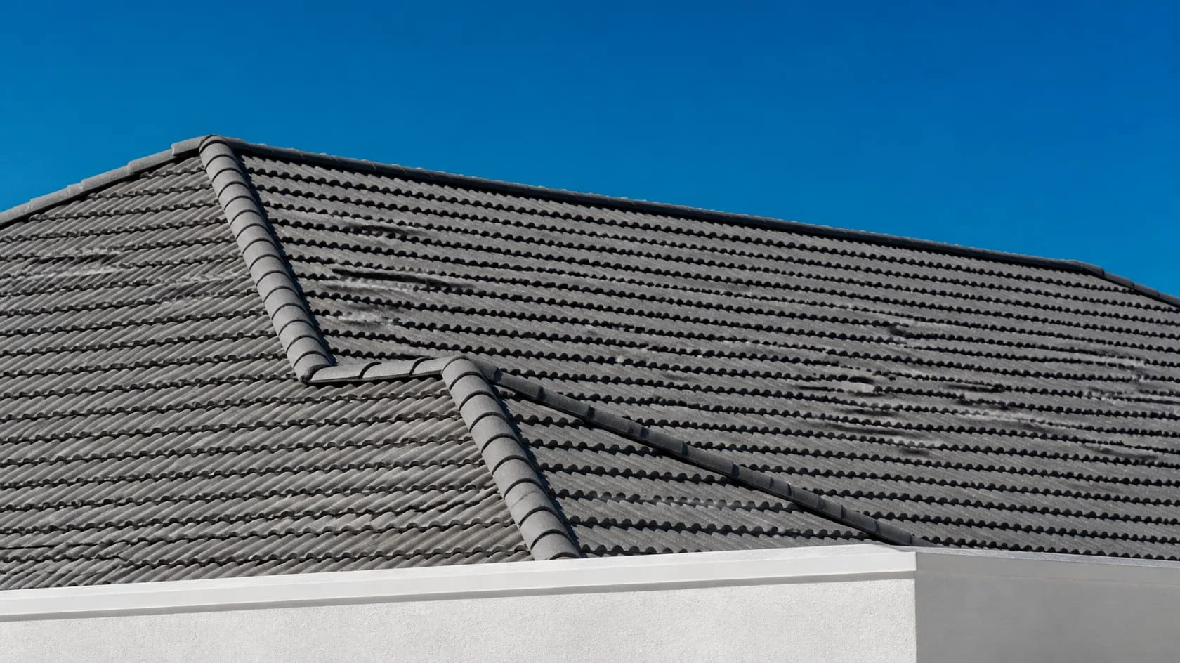 Slate gray tile roof with ridge caps beside a white wall