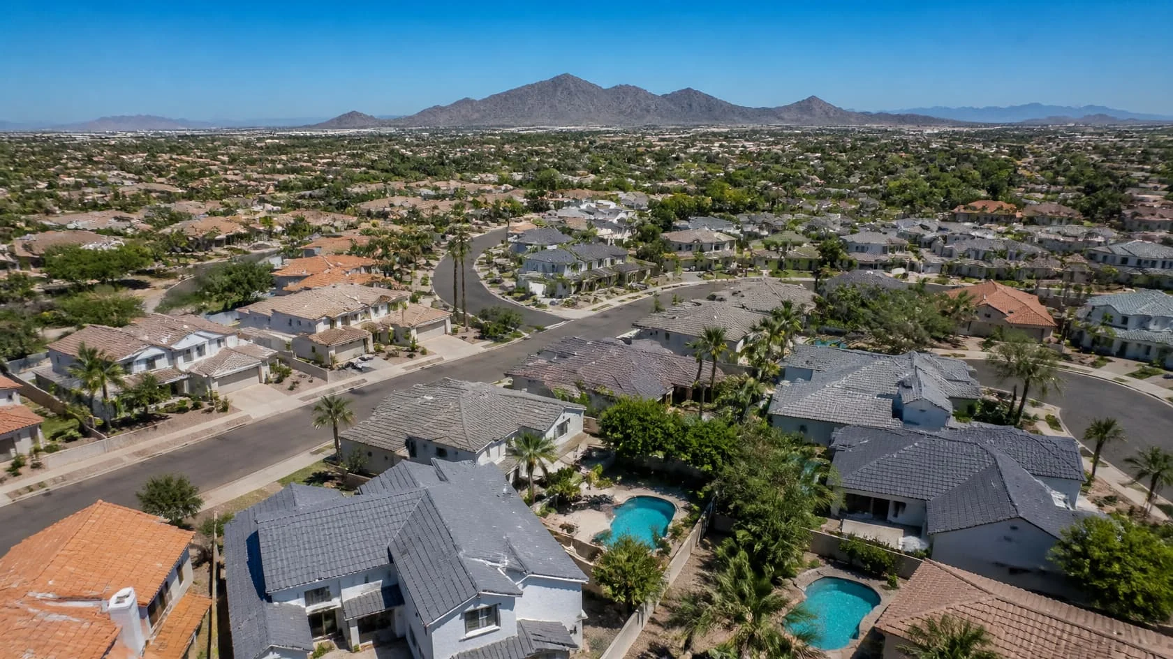 Aerial neighborhood of tile roofs, pools and distant mountains