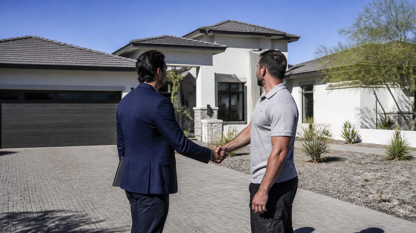 Two men shaking hands in a driveway outside a modern home